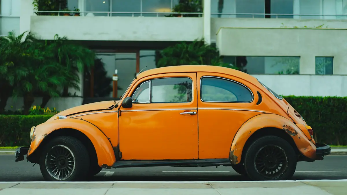 Weathered orange classic Volkswagen Beetle in profile on a city street