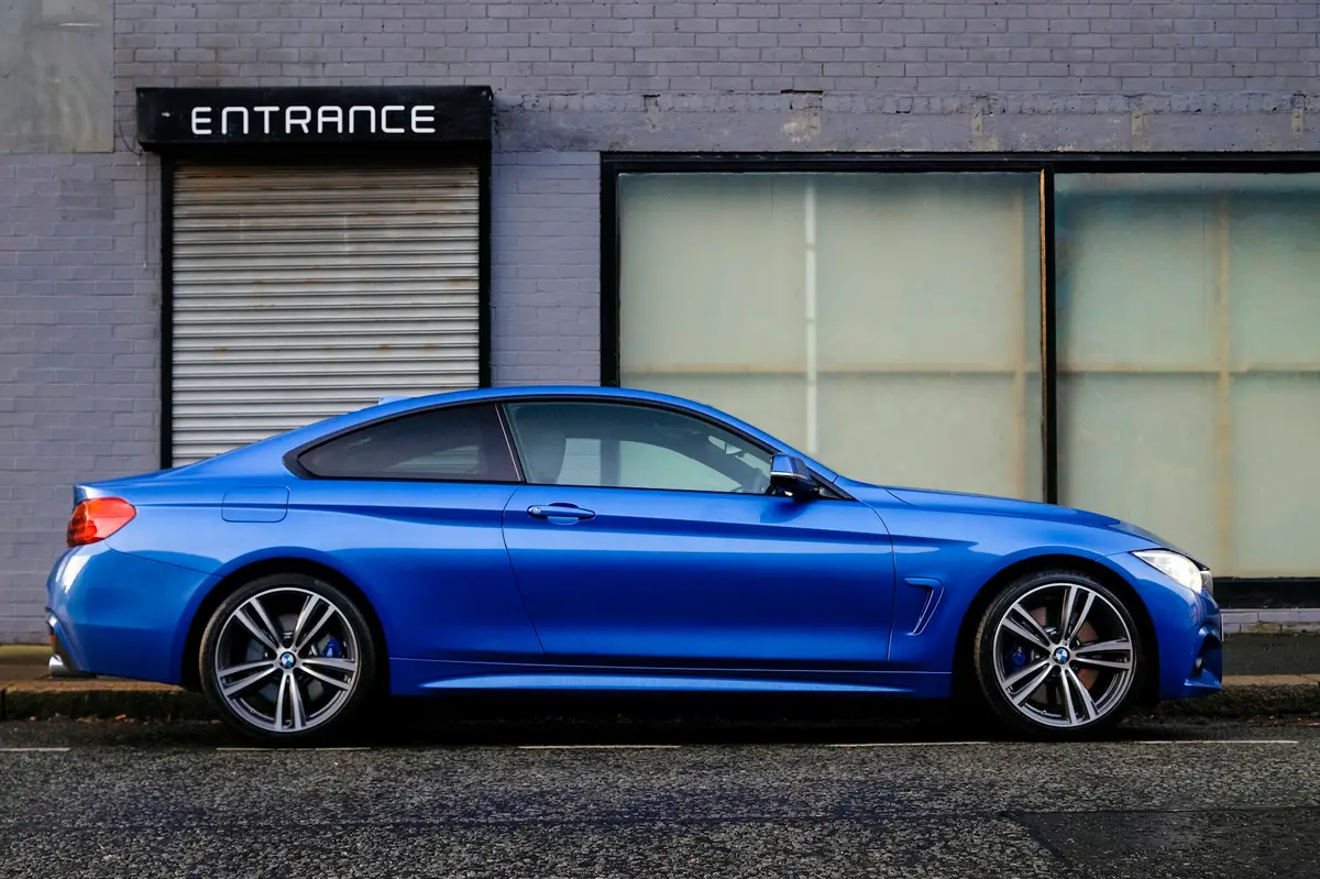 Blue BMW 4 Series coupe in perfect profile against a grey brick industrial wall