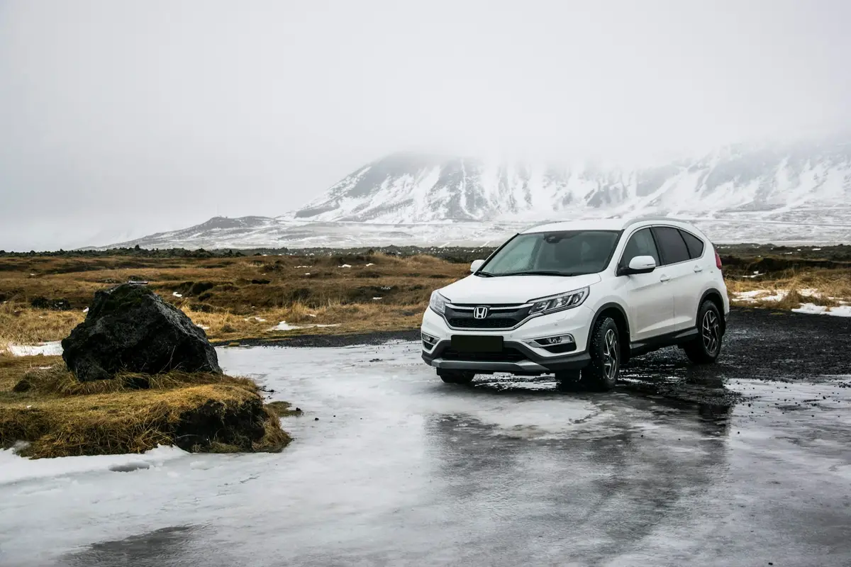 White Honda CR-V parked on icy ground with fog-covered winter hills behind